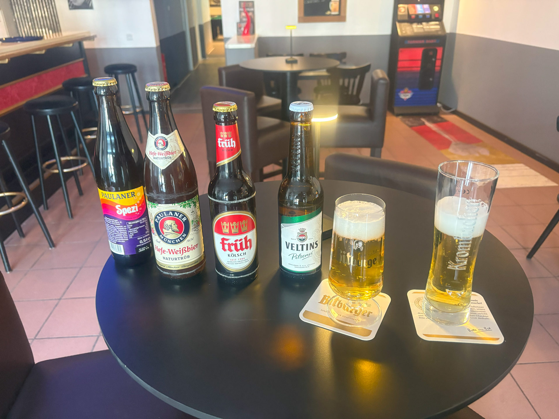 Fünf Bierflaschen und zwei gefüllte Biergläser auf einem schwarzen Tisch.